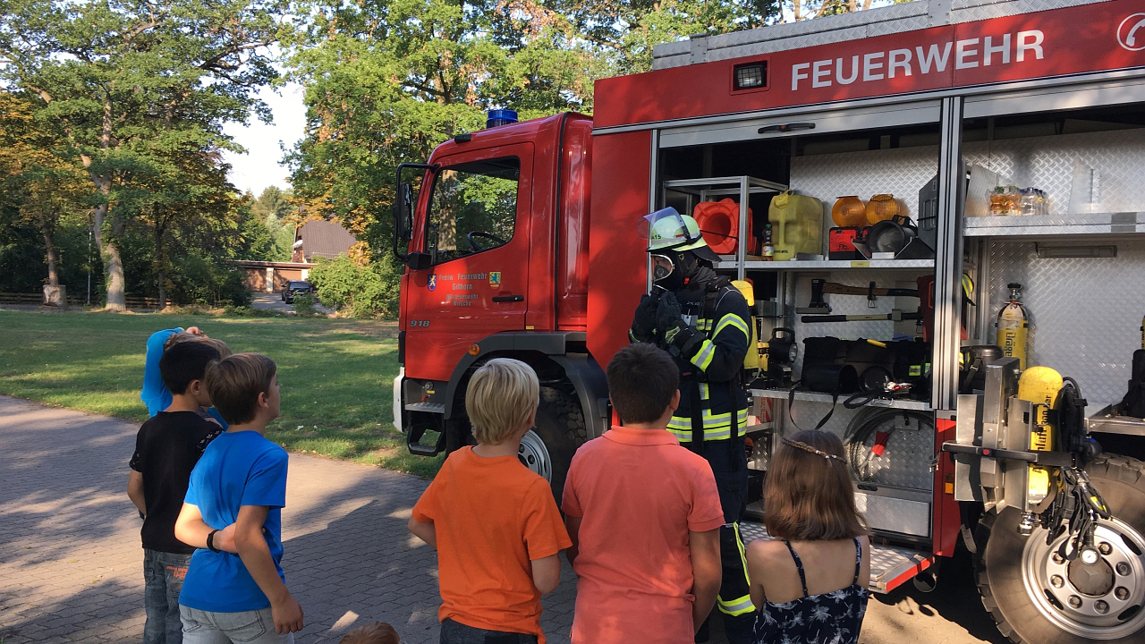 Feuerwehrmann erklärt den Kindern das Feuerwehr-Einsatzfahrzeug
