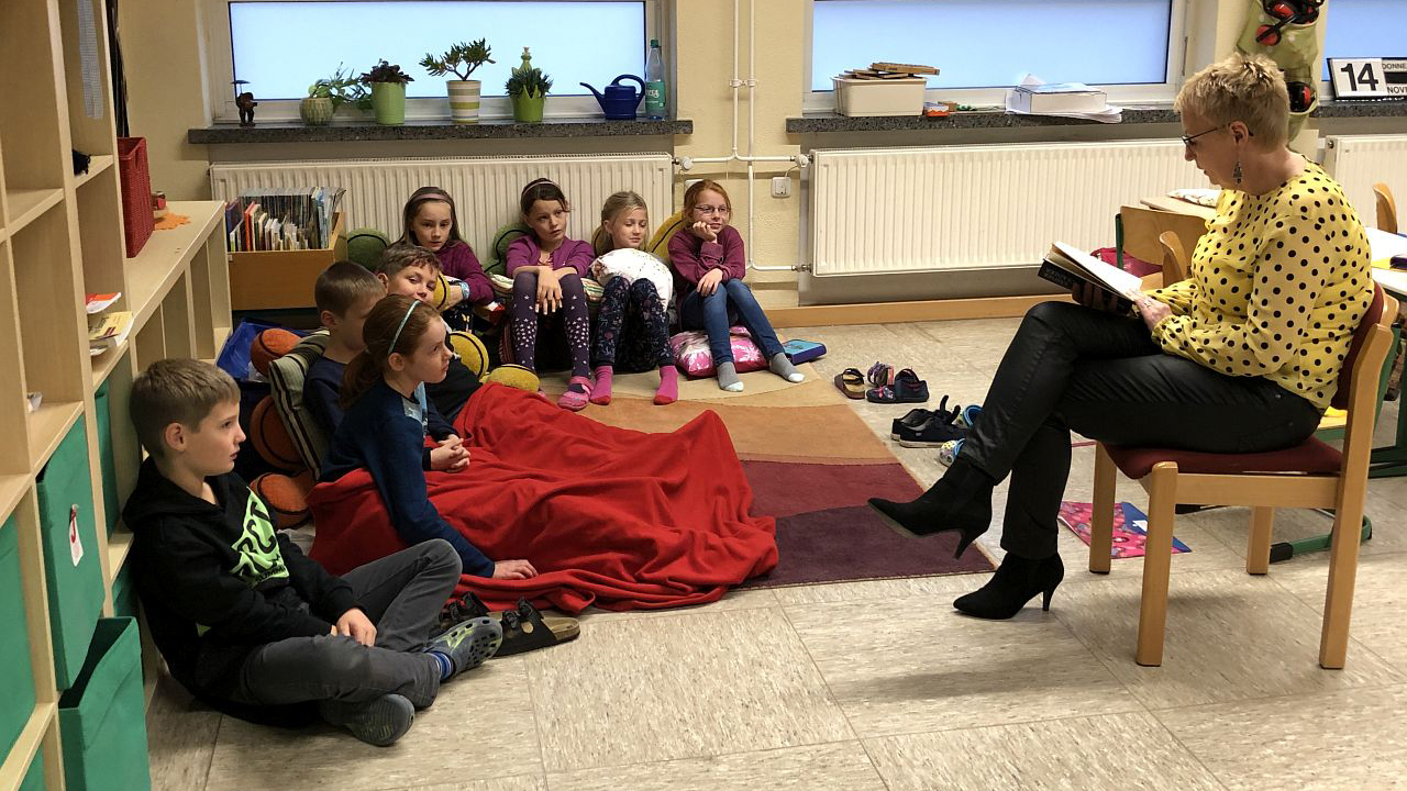 Eingekuschelt in Wolldecken lauschen Kinder der Vorleserin